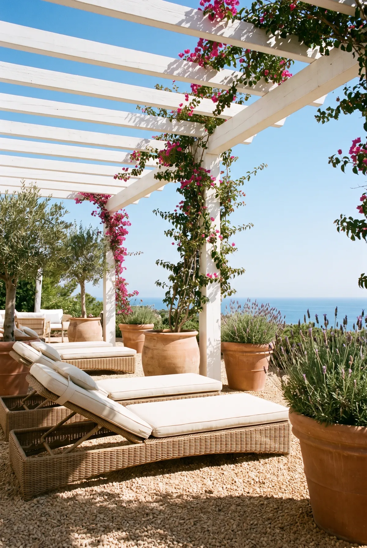 Coastal pea gravel patio under a white pergola with rattan loungers